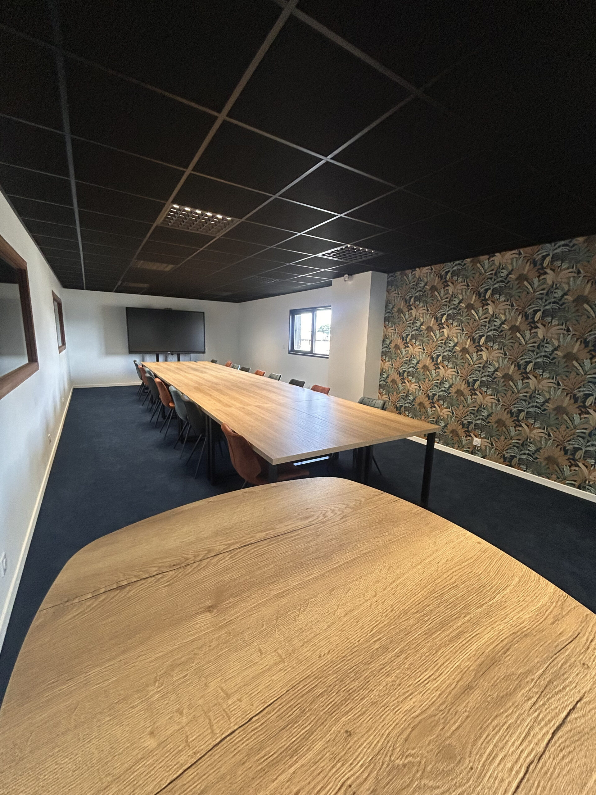Salle de réunion avec grande table en bois, écran tactile et papier peint végétal