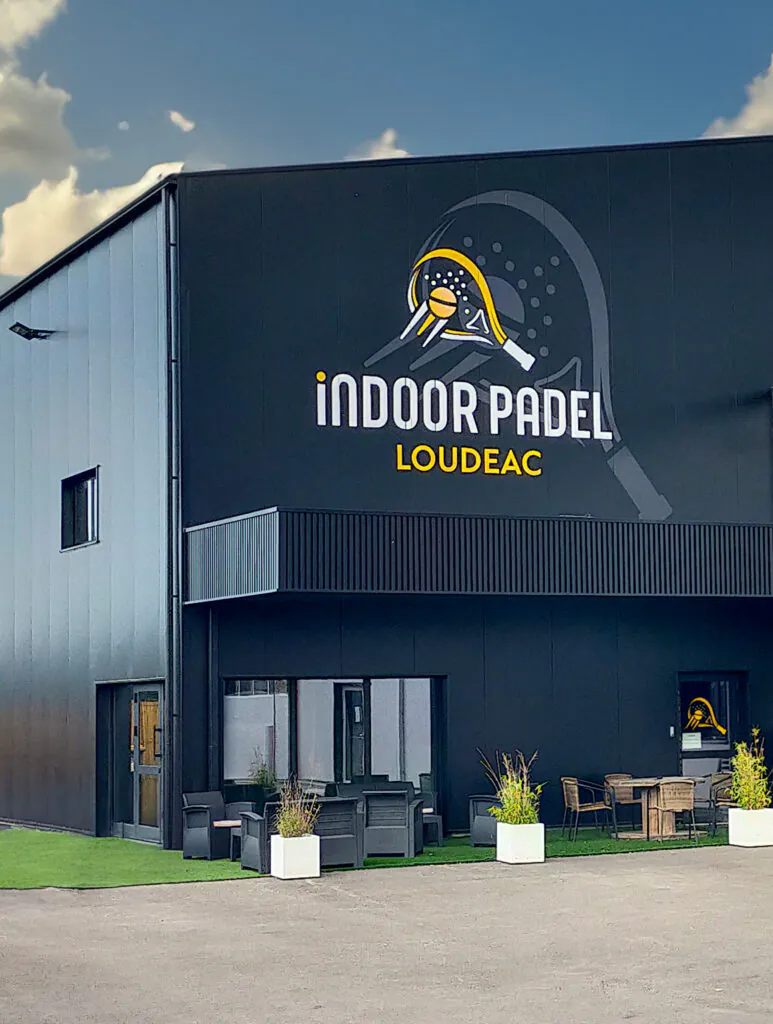Façade noire du club Indoor Padel à Loudéac avec terrasse aménagée et logo