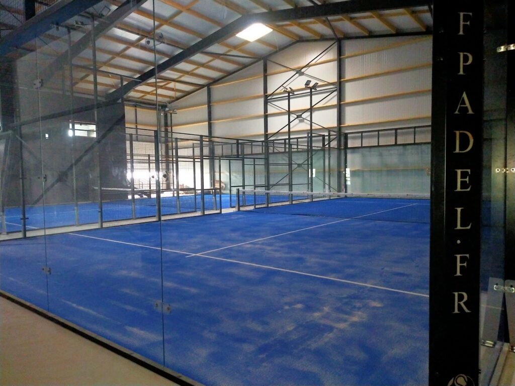Terrain de padel indoor au sol bleu avec vitres et grillage chez Indoor Padel Loudéac