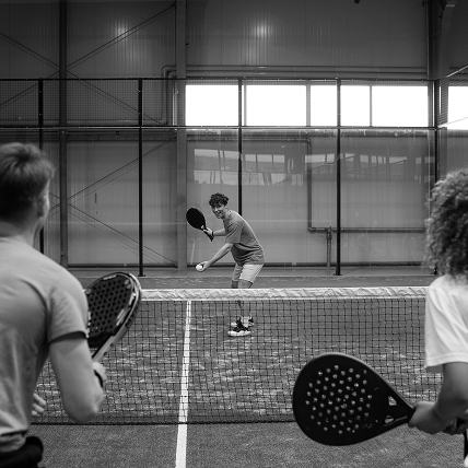 Joueur souriant prêt à servir lors d’une partie de padel indoor, photo en noir et blanc