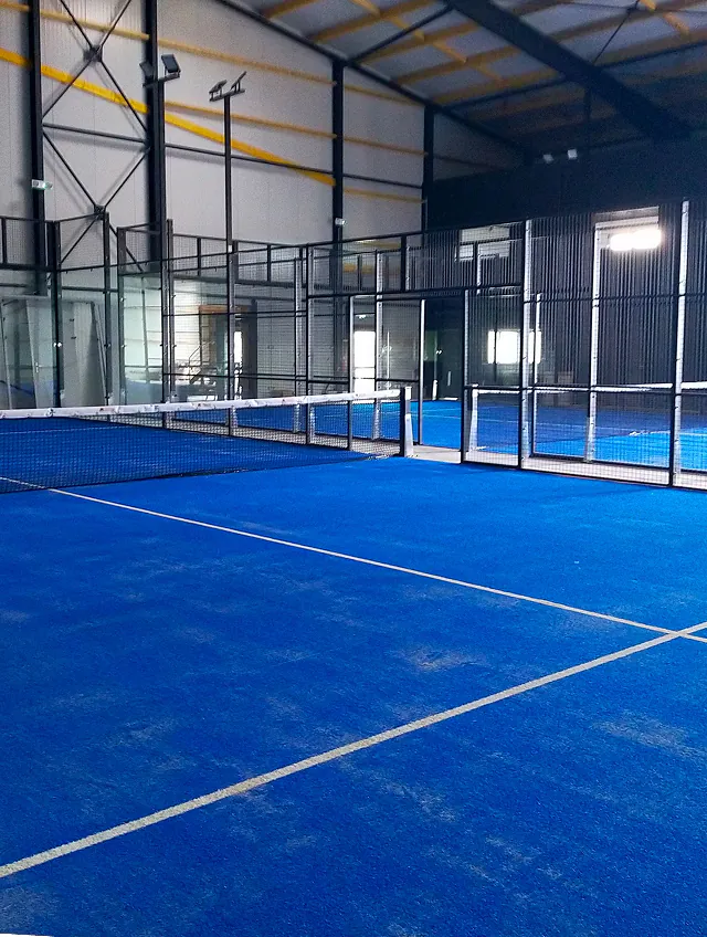 Terrain de padel indoor aux sols bleus, filet et parois vitrées dans le complexe Indoor Padel Loudéac